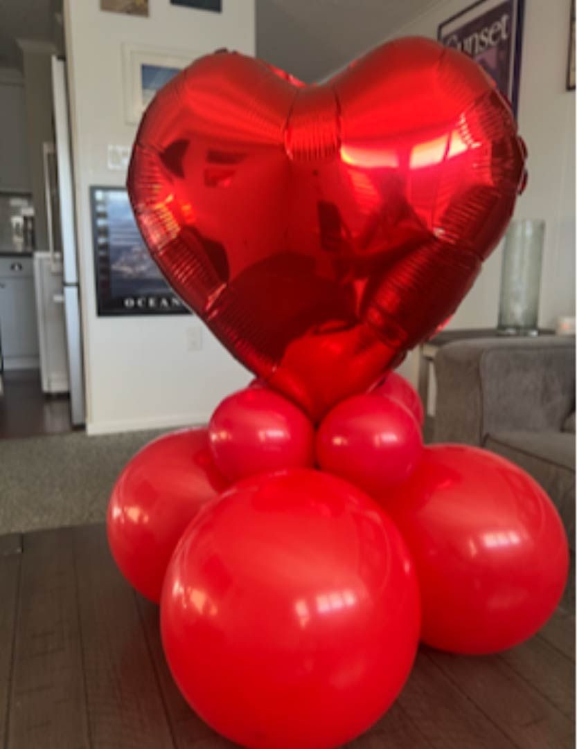 Red heart-shaped balloon centerpiece with round red balloons at the base in a living room setting.